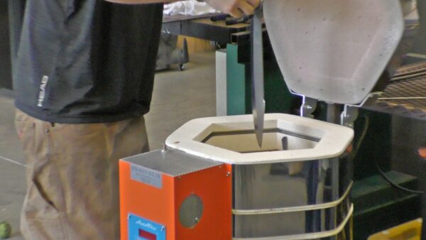 Man inserting a blade into a Jen-Ken Knife Kilns Vertical Air Bath 30 furnace